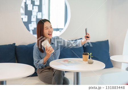 Connection and Sustainability. A joyful woman enjoying her coffee while taking a selfie in a modern cafe setting. 131883448