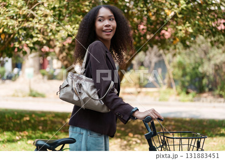 Eco-Conscious Commuting and Stylish Lifestyle. A woman with her bicycle smiling in a natural setting, advocating for a sustainable way to travel. Eco-Conscious Commuting and Stylish Lifestyle. A woman with her bicycle smiling in a natural setting, advocating for a sustainable way to travel. 131883451