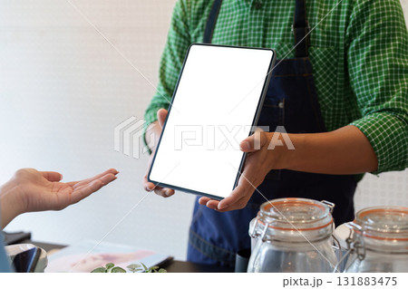 Technology and Green Solutions. A cafe employee demonstrating digital tools that promote sustainability in customer service. Technology and Green Solutions. A cafe employee demonstrating digital tools that promote sustainability in customer service. 131883475