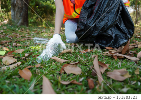 Promoting Eco-Consciousness. A volunteer diligently collects plastic bottles from the grass during a park cleanup campaign. 131883523