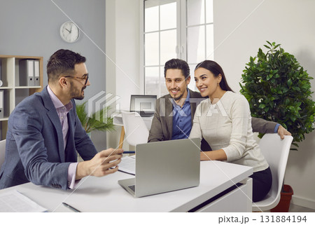 Happy couple sitting with a business broker or insurance agent showing project on a laptop screen. Happy couple sitting with a business broker or insurance agent showing project on a laptop screen. 131884194