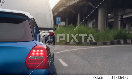 Rear side of mini car blue color with turn on brake light. Parking behind a cargo car. Side of car with curved asphalt road for U-Turn under level bridge. 131886427
