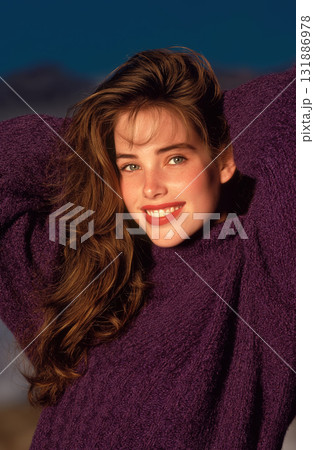 Young woman smiling in purple sweater with long brown hair and warm sunlight on face conveying relaxed confidence 131886978