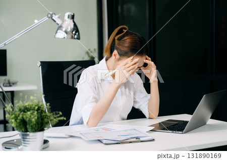 Asian woman feeling migraine head strain.Overworked businesswoman financier while working on laptop and tablet 131890169