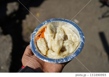Close up of Hand Holding Steamed Momos Dumplings with Spicy Dipping Sauce Close up of Hand Holding Steamed Momos Dumplings with Spicy Dipping Sauce 131890993