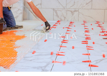 Worker applies adhesive arranges tiles with clips for precise spacing clean finish. 131891368