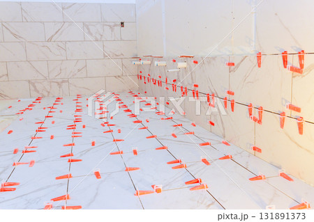 Workers are laying white marble tiles on bathroom floor, wall, preparing for stylish finish. Workers are laying white marble tiles on bathroom floor, wall, preparing for stylish finish. 131891373