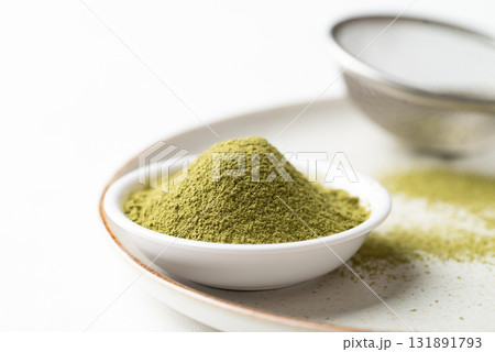 Matcha green tea powder in bowl and sieve on plate with white background Matcha green tea powder in bowl and sieve on plate with white background 131891793