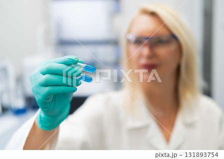 Blonde woman in lab coat studying blue liquid in test tube in chemistry lab. Blonde woman in lab coat studying blue liquid in test tube in chemistry lab. 131893754