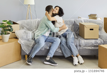 Happy couple hugging on sofa with moving boxes, celebrating new home together 131894746
