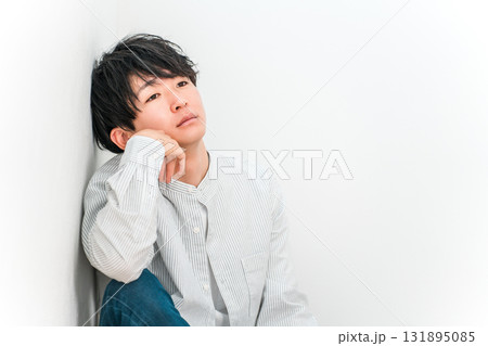 白い壁のリビングに頬杖をついて座る若いアジア人男性(落ち込む,無気力,脱力,現実逃避) 白い壁のリビングに頬杖をついて座る若いアジア人男性(落ち込む,無気力,脱力,現実逃避) 131895085