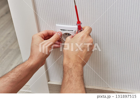 electrician installing electrical socket in white plastic frame with a screwdriver at home 131897515