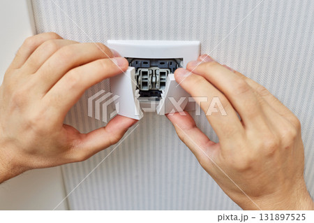male hands of electrician installing white two-key electric light switch at home. Replacing. 131897525