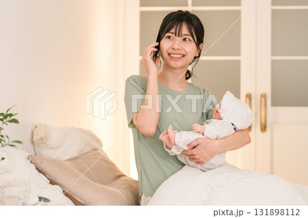 寝室,ベッドルームで赤ちゃんを抱っこしながらスマホで通話する若いアジア人女性 寝室,ベッドルームで赤ちゃんを抱っこしながらスマホで通話する若いアジア人女性 131898112