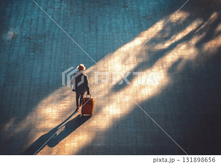 Person traveling with luggage walking through sunlight and shadows 131898656