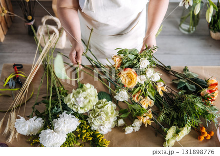 Woman assembling a bouquet with yellow rose and greenery in a seasonal floristry setting. Mindful crafting, slow floristry, bouquet making workshop, creative floral hobby 131898776