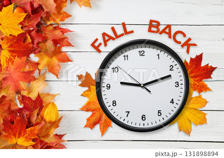Clock set against a white wooden background with autumn leaves 131898894