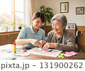 介護士と高齢女性が笑顔で工作を楽しむデイサービスの風景 131900262