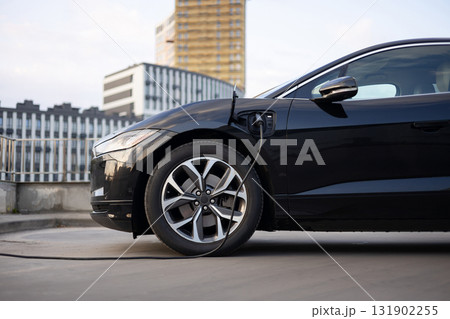 A black electric vehicle is plugged in and charging in an urban setting. 131902255