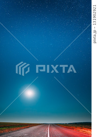 Night Starry Sky With Moon Above Country Asphalt Road In Countryside. Night View Of Natural Glowing Stars. Ground In Lights From Rear Red Car Lights Night Starry Sky With Moon Above Country Asphalt Road In Countryside. Night View Of Natural Glowing Stars. Ground In Lights From Rear Red Car Lights 131902921
