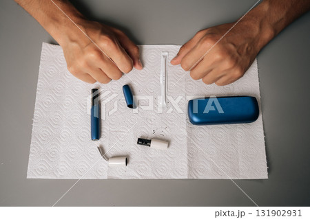 Close-up top view of unrecognizable man cleaning electronic cigarette with cleaning stick and paper on table, performing maintenance, ensuring proper hygiene, sanitizing personal vaping equipment. 131902931