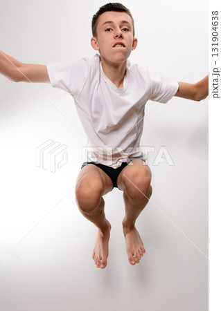 Teenager mid-jump, arms outstretched, wearing a white shirt and dark shorts against a white background. Teenager mid-jump, arms outstretched, wearing a white shirt and dark shorts against a white background. 131904638