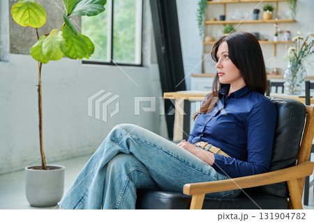 Serious young woman sitting in chair at home 131904782