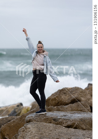 Woman raising arm on coastal rocks enjoying sea waves 131906156