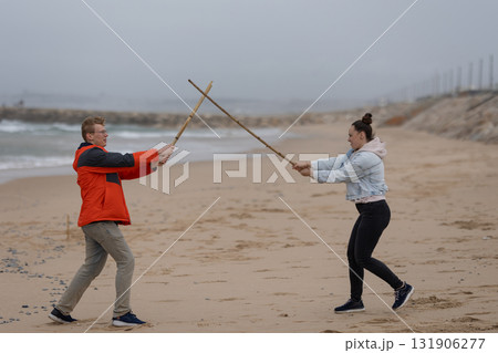 Couple playing sword fighting game on sandy beach Couple playing sword fighting game on sandy beach 131906277