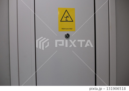 Warning sign displayed on door in public transport vehicle, cautioning passengers to watch their step. Safety and awareness, providing visual guide for preventing accidents 131906518