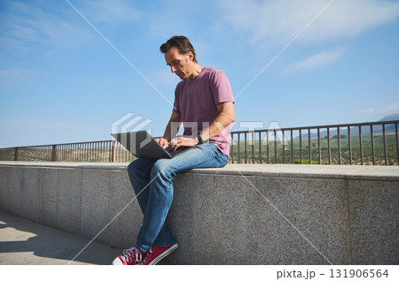 Focused Man Working On Laptop Outdoors On A Sunny Day, Casual Style, Scenic Hilltop View Focused Man Working On Laptop Outdoors On A Sunny Day, Casual Style, Scenic Hilltop View 131906564