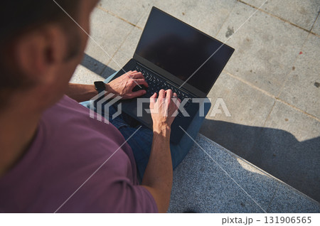 Outdoor Laptop Work: Man Typing On A Sleek Laptop While Sitting On Concrete Steps, Capturing Focused, Casual Technology Use 131906565