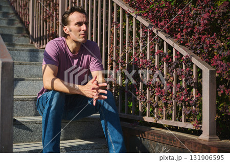 Thoughtful Man In Casual Purple Shirt Sitting On Outdoor Stairs By Railings Thoughtful Man In Casual Purple Shirt Sitting On Outdoor Stairs By Railings 131906595
