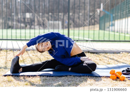 Young woman stretching on yoga mat, enjoying outdoor workout near sports field Young woman stretching on yoga mat, enjoying outdoor workout near sports field 131906660