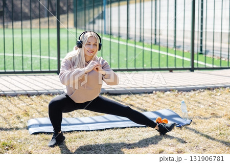 Young woman stretching legs and listening music with headphones during outdoor workout Young woman stretching legs and listening music with headphones during outdoor workout 131906781