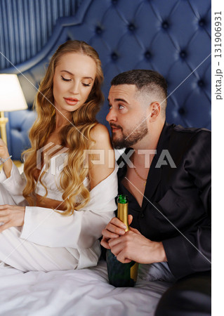 A man and a woman in silk pajamas with champagne are lying on a bed. 131906931