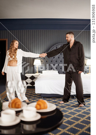 A man and a woman in silk pajamas dancing in the bedroom. breakfast in the hotel A man and a woman in silk pajamas dancing in the bedroom. breakfast in the hotel 131906988