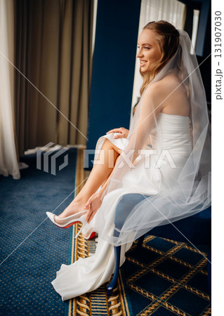 The bride in simple beautiful elegant wedding dress puts on shoes 131907030