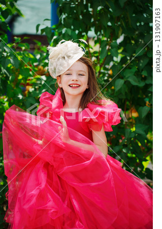A girl in a lush pink dress and hat near the green bushes 131907163