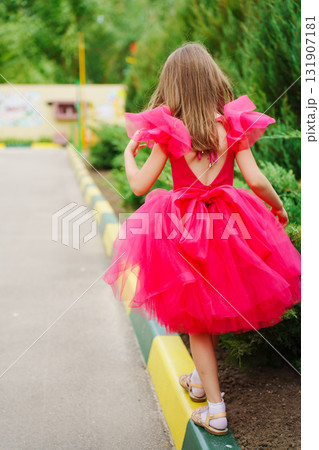 A girl in a lush pink dress and hat on a walk. view from the back 131907181