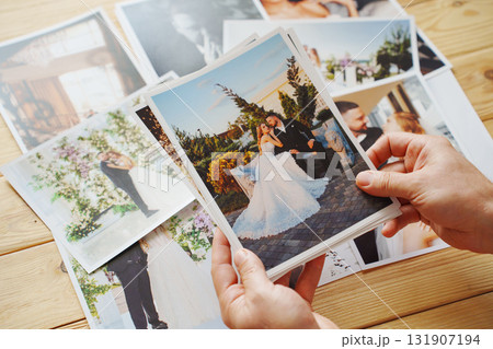 Men's hands put on the wooden table and show wedding photos. Men's hands put on the wooden table and show wedding photos. 131907194