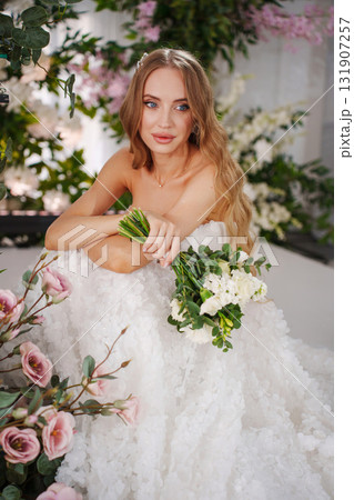 Beautiful bride with long blonde hair sitting surrounded by flowers. Beautiful bride with long blonde hair sitting surrounded by flowers. 131907257