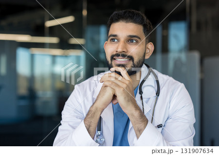 Indian male doctor wearing a white lab coat and stethoscope, thoughtfully looking away, representing medical contemplation and professional aspiration in a clinic setting Indian male doctor wearing a white lab coat and stethoscope, thoughtfully looking away, representing medical contemplation and professional aspiration in a clinic setting 131907634
