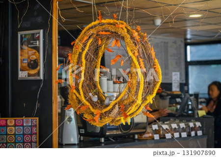 Autumn themed wreath with orange leaves and yellow yarn hangs in cozy cafe window. Concept of Thanksgiving, Halloween, seasonal decoration, cozy ambiance, fall atmosphere Autumn themed wreath with orange leaves and yellow yarn hangs in cozy cafe window. Concept of Thanksgiving, Halloween, seasonal decoration, cozy ambiance, fall atmosphere 131907890