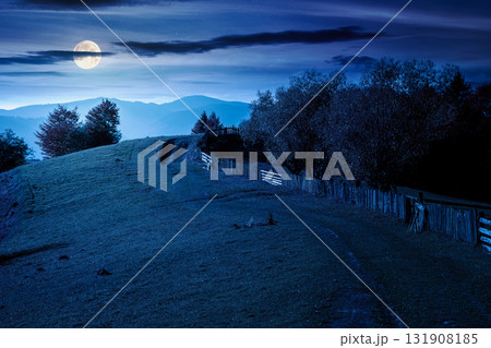 mountainous rural landscape in autumn at night. field behind the wooden fence in full moon light. scenery in fall season. forest on the hill. ridge in the distance 131908185