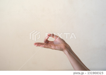 A close-up of a human hand making an 'OK' gesture against a neutral background. Gyan mudra. The hand is of a young adult with light skin and slender fingers. 131908323