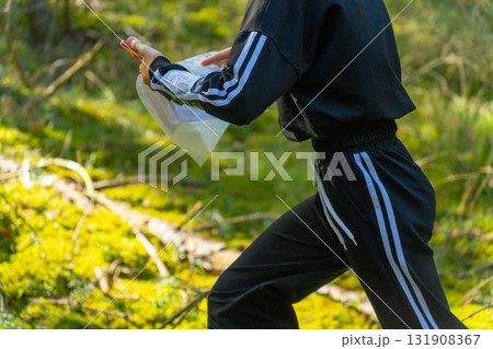 Orienteering athlete running through a summer forest with a map and compass. 131908367