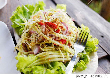 Thai spicy mango salad with crispy fish and vegetable in white dish on wooden table 131908369