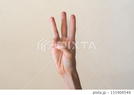 A hand with a light skin tone is raised, showing the number three with fingers extended. The background is a neutral color, emphasizing the gesture. 131908549