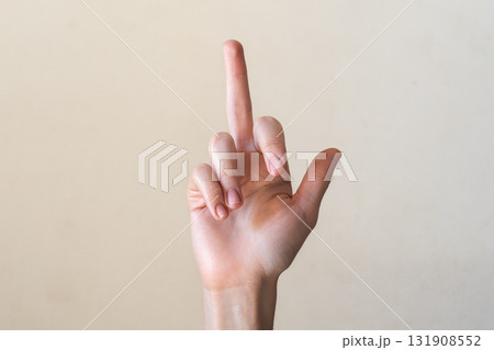 A close-up of a human hand showing a raised middle finger. The hand is pale with well-groomed nails. The background is a neutral color, creating a simple composition. 131908552